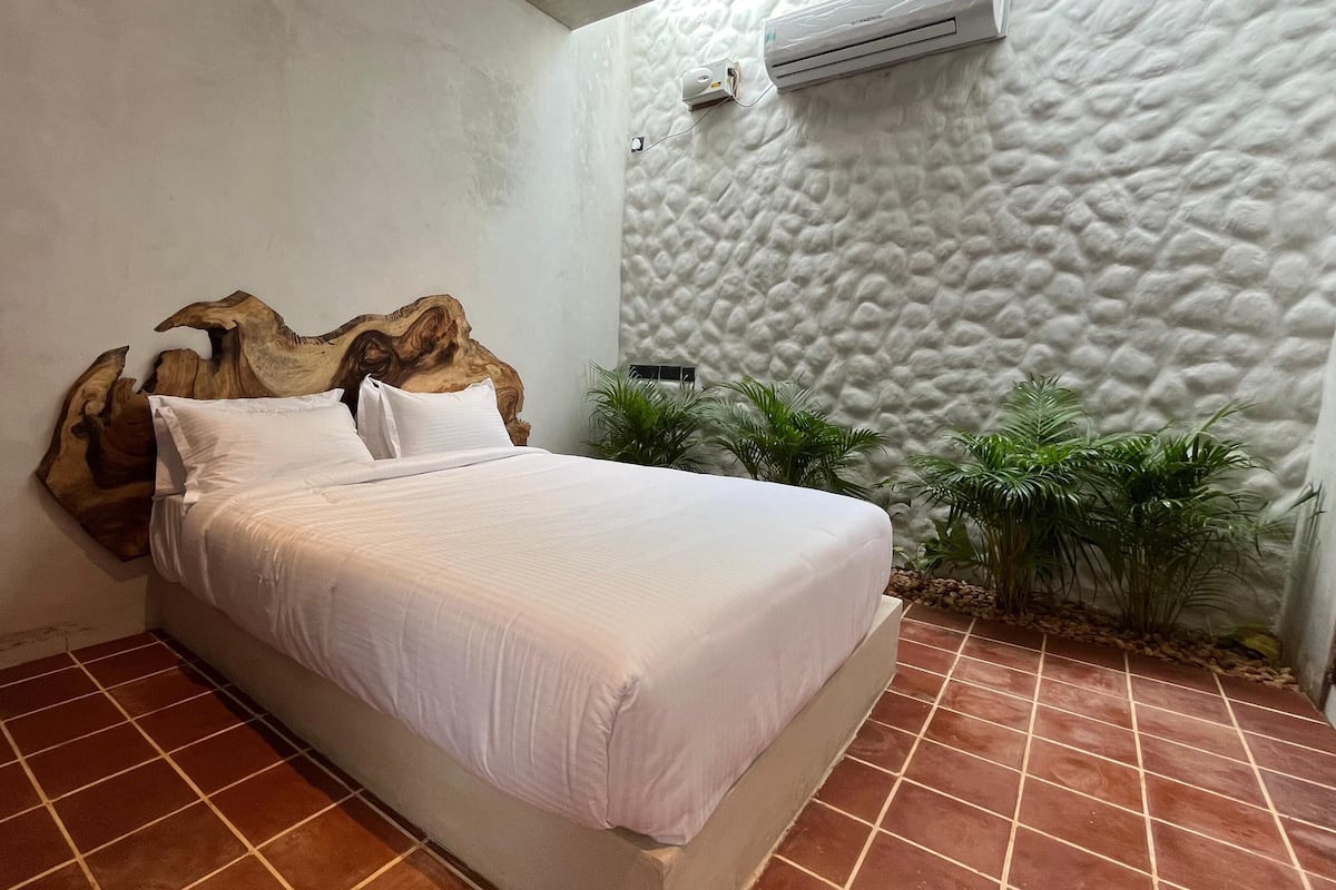 Un dormitorio con cama, pared con textura y planta en maceta.