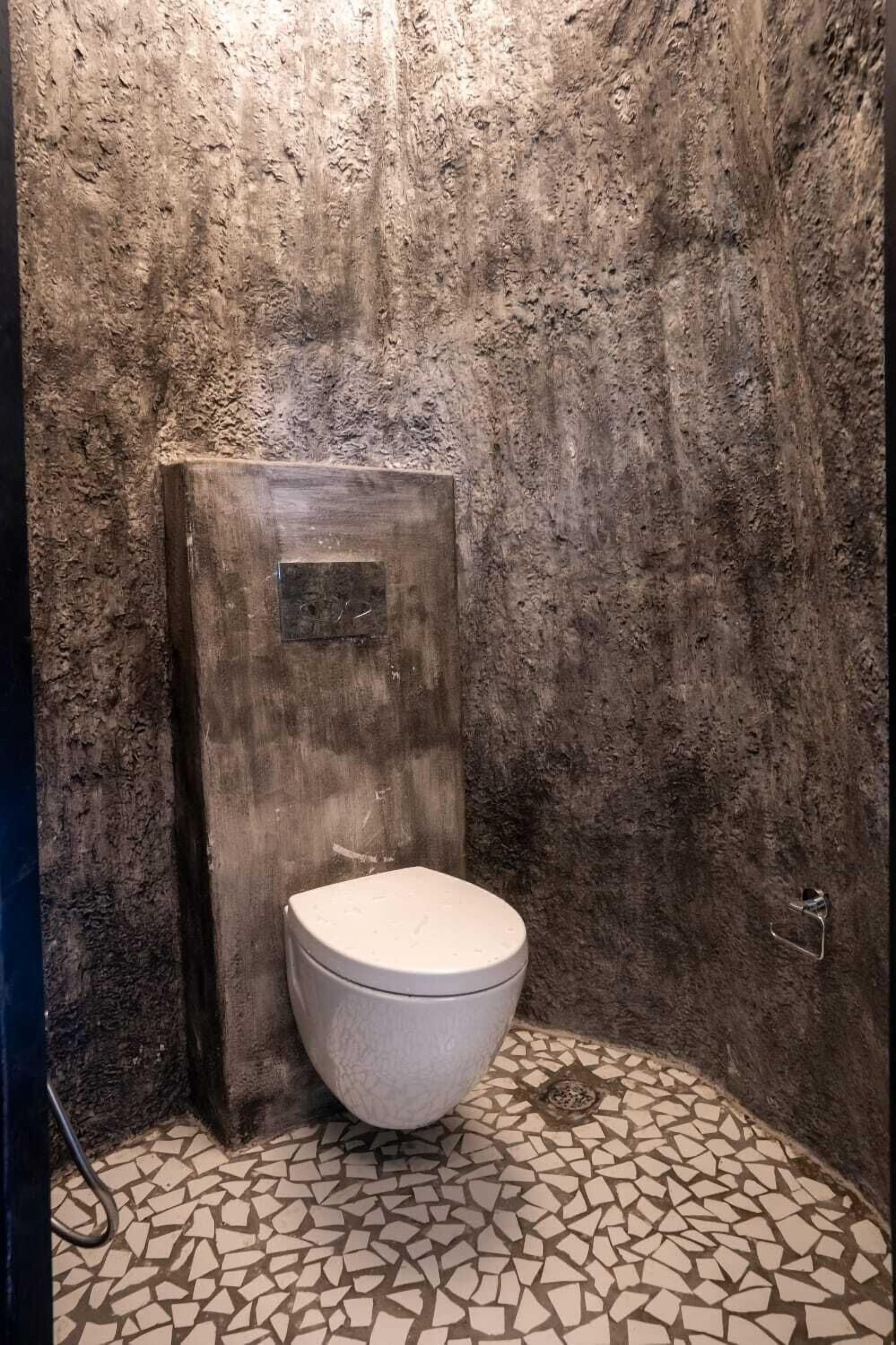 Un baño con pared texturizada, puerta de madera y suelo de baldosas.
