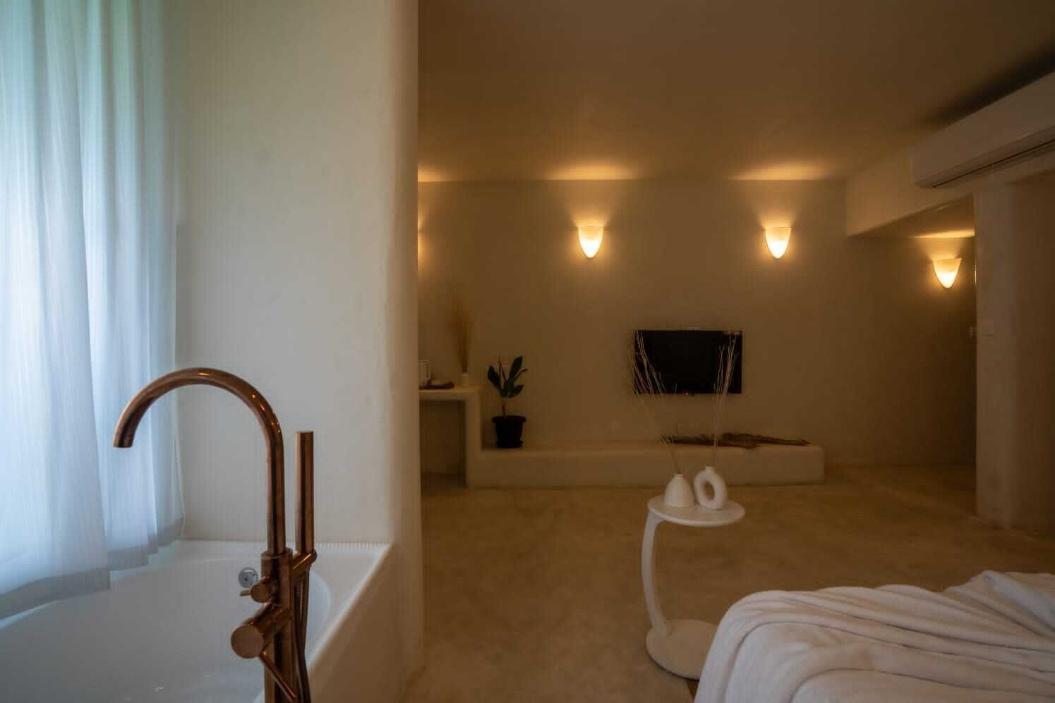 A modern, minimalist bedroom with a large window, a bathtub, a small white table, and wall-mounted sconces.