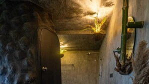 A stone-walled bathroom with a textured floor, a black door, a sink with a bowl, and a hanging plant. - Nomads Resort - Destination Stays (Vanur)