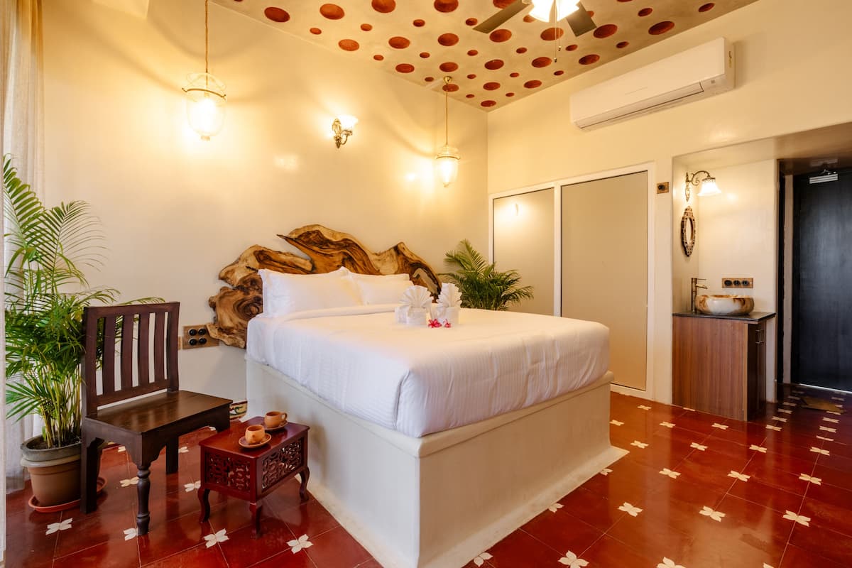 Habitación de hotel con una cama grande, una silla de madera, una mesita con una planta y un techo decorativo.