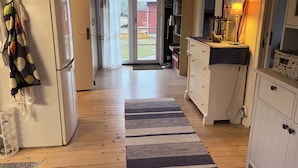 A kitchen with a refrigerator, a wooden floor, a striped rug, and a door leading to a backyard. - Nice cottage located in the north of Öland next to Byxelkrok | SE04024 (Byxelkrok)