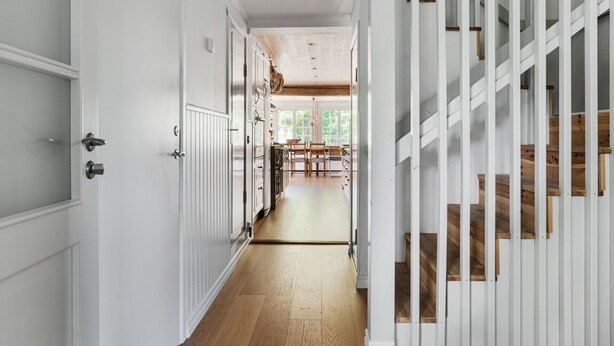 Un pasillo con puertas blancas, piso de madera y una escalera con escalones de madera.