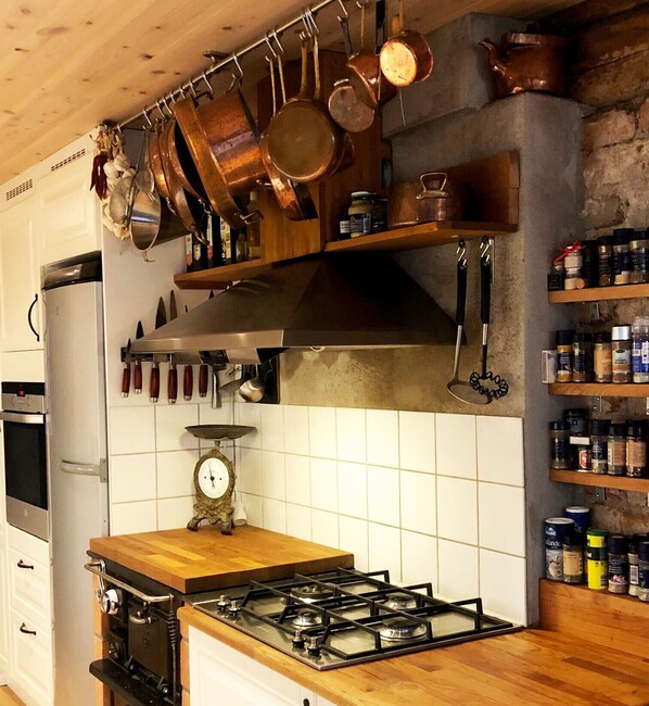 A kitchen with a gas stove, hanging pots, a scale, and shelves with jars.