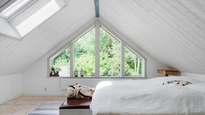 Un dormitorio con techo inclinado, un ventanal grande, una cama, un radiador y un banco de madera.