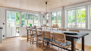 Un comedor con mesa y sillas de madera, ventanas amplias y un colgador de luces.