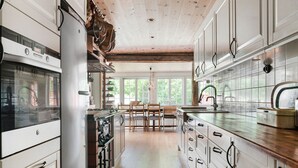 Una cocina con armarios blancos, techo de madera y un comedor con sillas y una mesa.