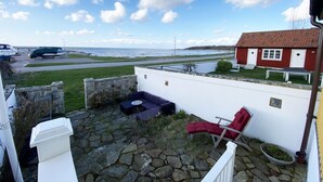 A stone patio with a white wall, a red chair, and a white building with a red roof in the background.