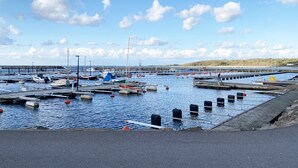 A marina with boats docked at wooden piers, a sandy beach in the background, and a clear sky with clouds.