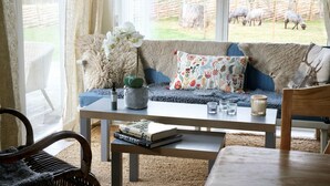 A cozy living room with a sofa, a coffee table, and a view of a fenced outdoor area with sheep.