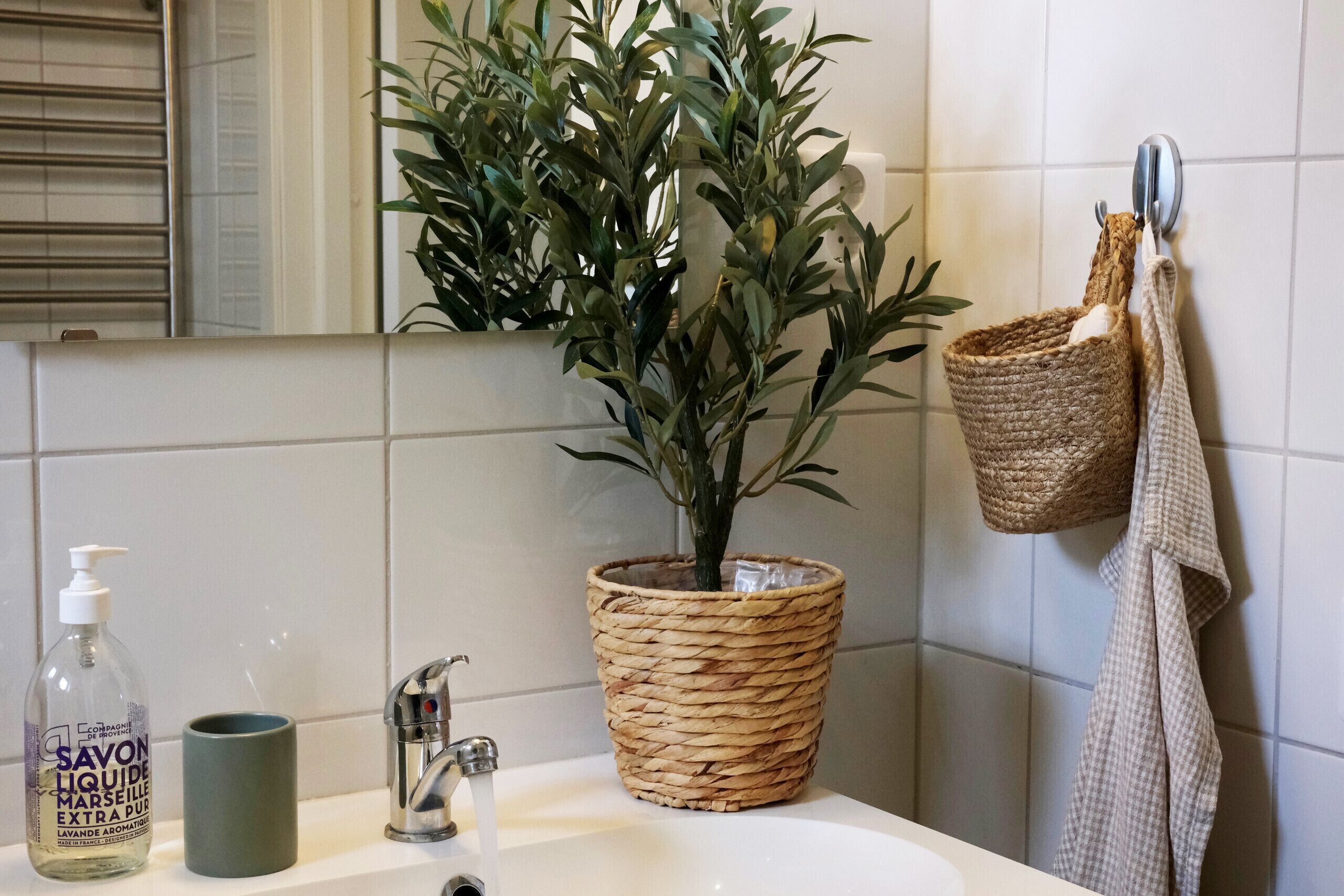 A bathroom with a sink, a potted plant, a bottle of soap, a towel, and a basket.