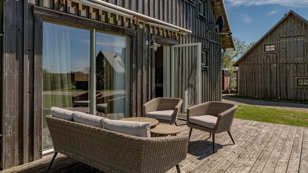A wooden building with large glass doors, wicker furniture, and a clear view of the surrounding area.
