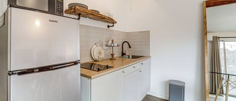 Een moderne keuken met een Galanz koelkast, een houten plank boven de gootsteen, een roestvrijstalen spoelbak en een grijze prullenbak.