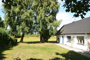 Ein Haus mit geneigtem Dach, heller Fassade und einem Fenster mit blauem Klappladen.