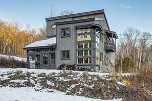 Un edificio moderno de varios pisos con amplias ventanas y techo inclinado, rodeado por un paisaje nevado y árboles.