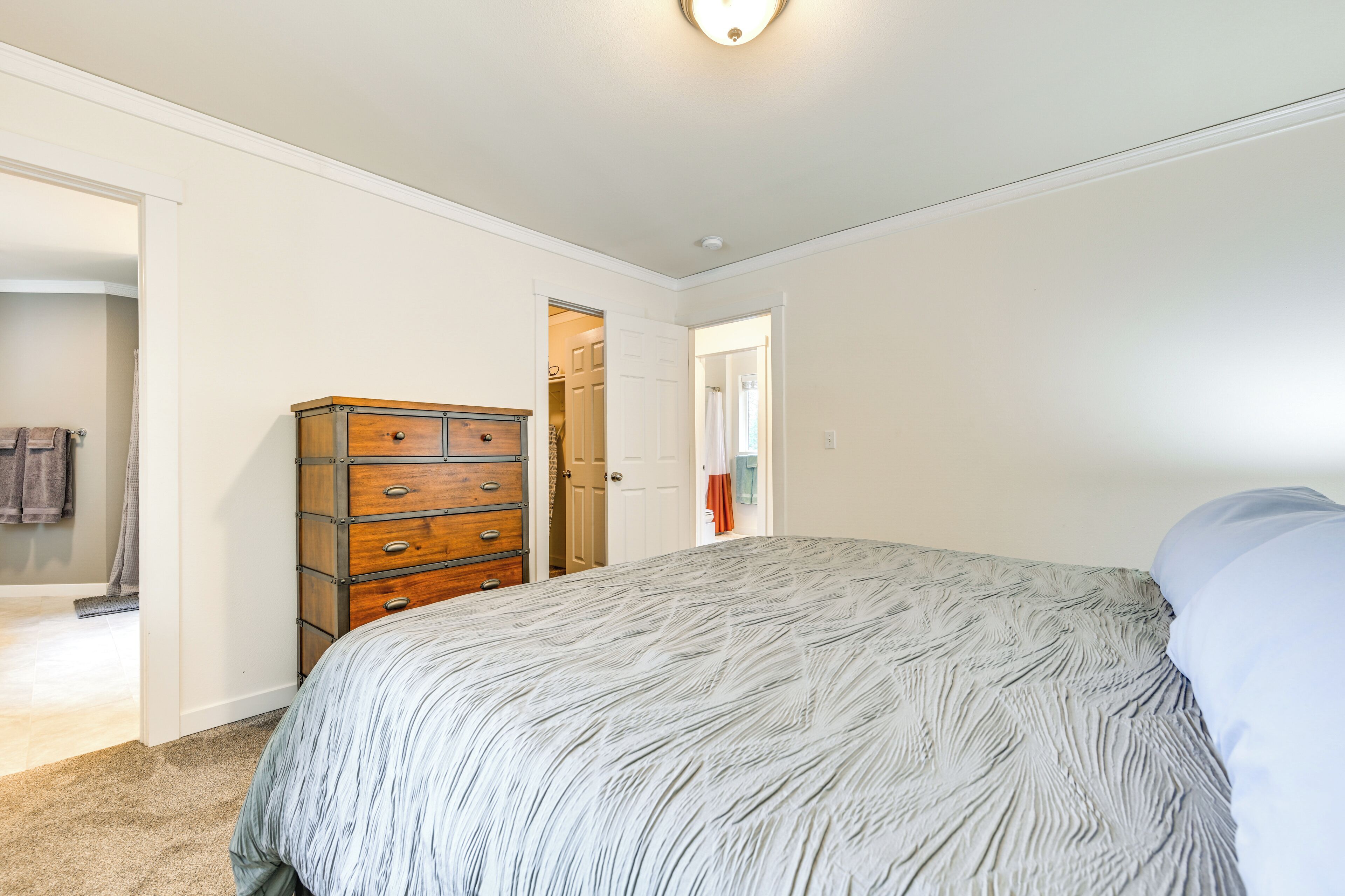 A bedroom with a large bed, a wooden dresser, and a door leading to another room.