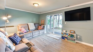A living room with a grey sofa, a coffee table, a flat-screen TV mounted on the wall, and a sliding glass door leading to an outdoor area. - Lakefront Gem w/ Deck & Grill in Shelton (Shelton)