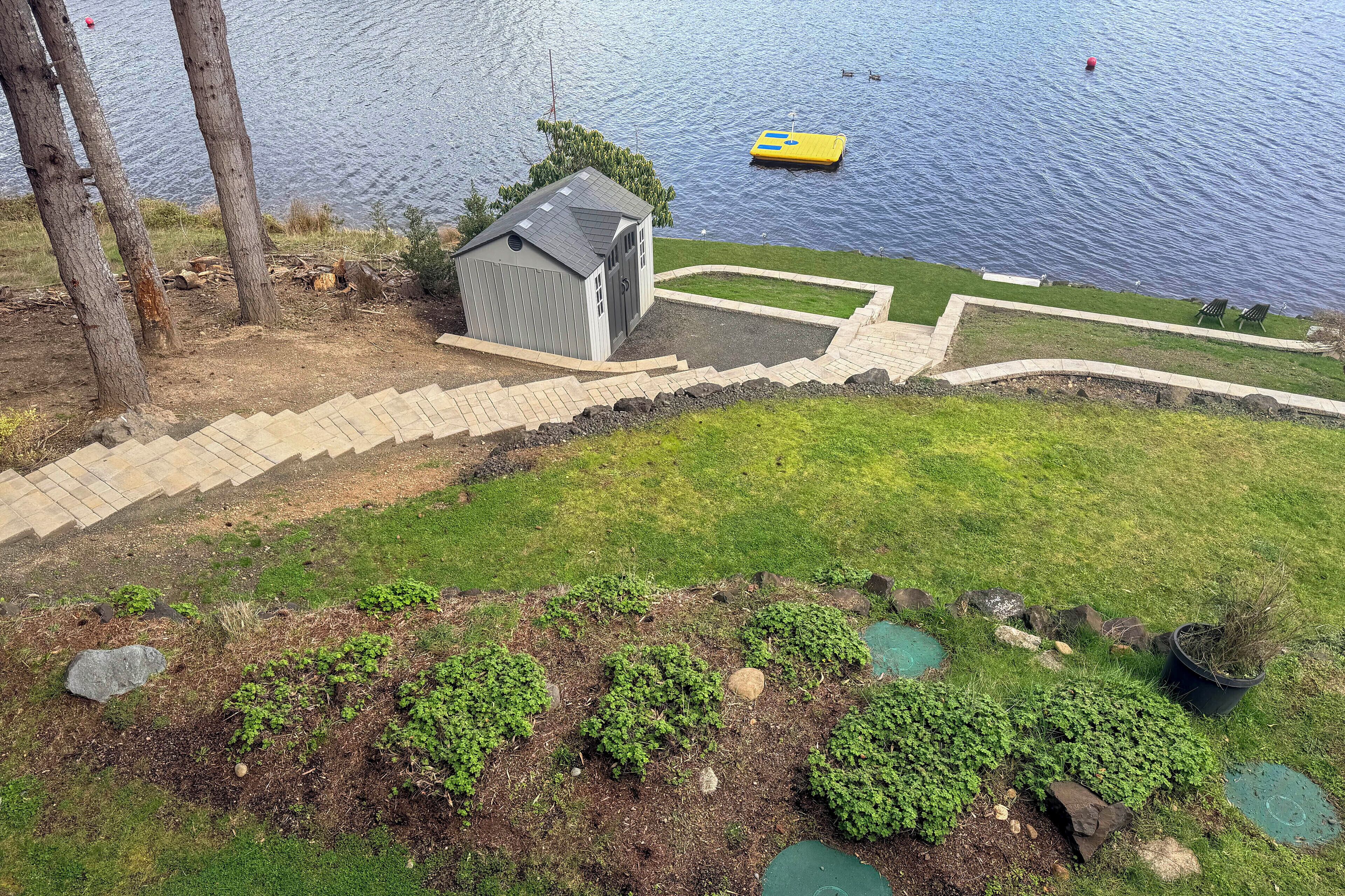 Una propiedad junto al lago, con un cobertizo pequeño, una terraza pavimentada y un muelle para barcos.