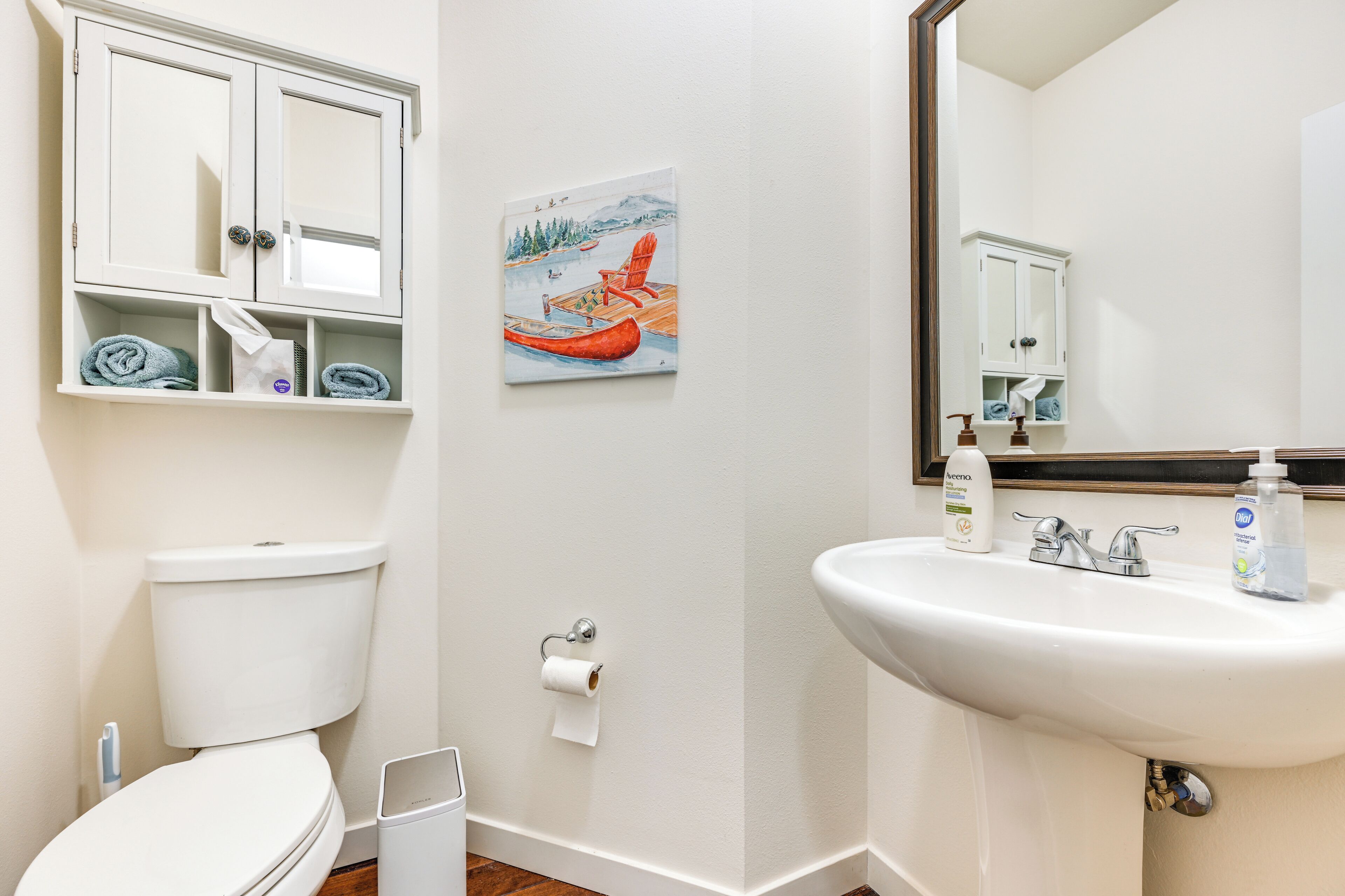 Une salle de bain avec des toilettes, un lavabo et un tableau représentant un canoë amarré à un quai.
