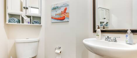 Une salle de bain avec des toilettes, un lavabo et un tableau représentant un canoë amarré à un quai.