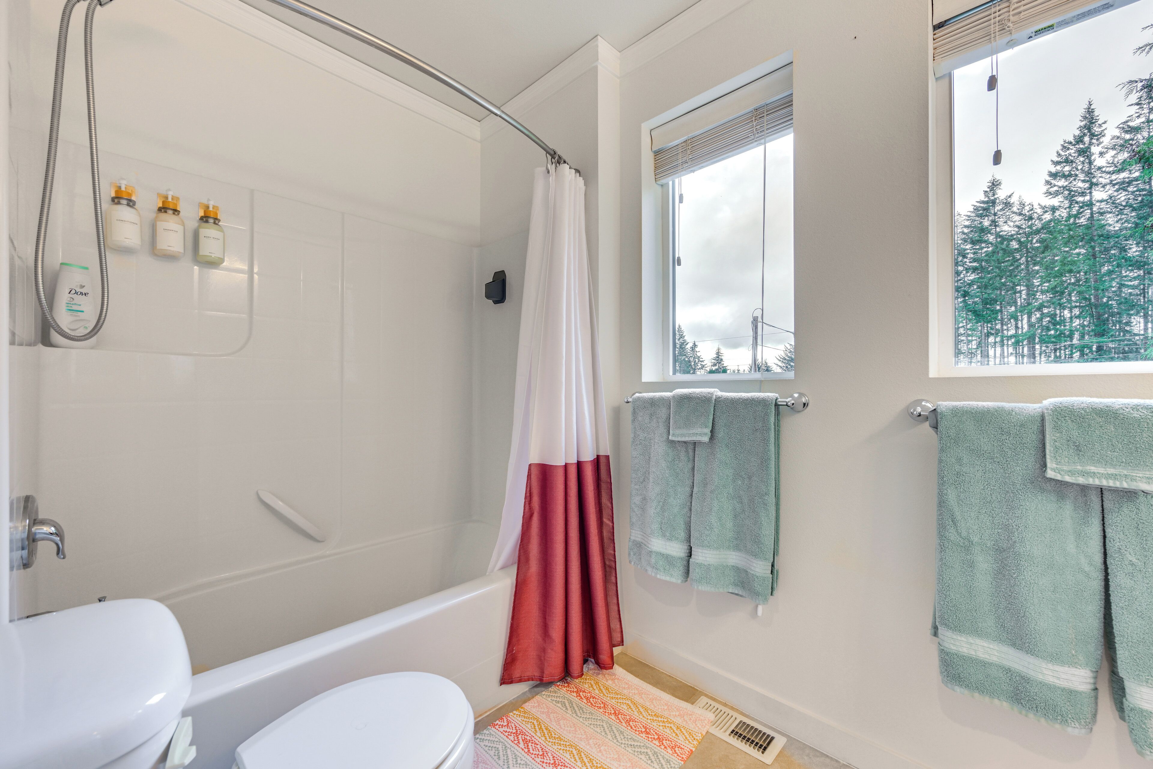 A bathroom with a bathtub, a toilet, a shower curtain, and a window with a view of trees.