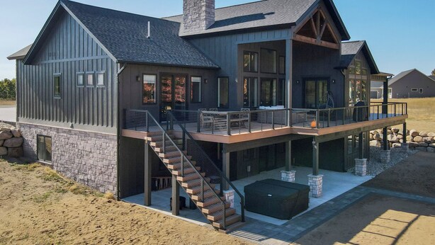A modern two-story house with a stone foundation, large windows, and a covered outdoor area.