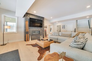 A modern living room with a fireplace, a mounted TV, a sofa, and a staircase. - Boyne Mtn Retreat w/ Hot Tub + Shuttle to Resort! (Boyne Falls)
