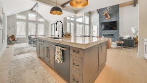 A spacious kitchen with a large island, pendant lighting, and a stone fireplace.