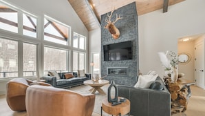 A modern living room with a stone fireplace, leather sofas, and a mounted deer head.