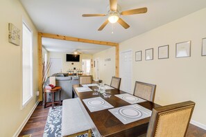 Un comedor con una mesa de madera preparada para cuatro personas, un ventilador de techo y certificados enmarcados en la pared.