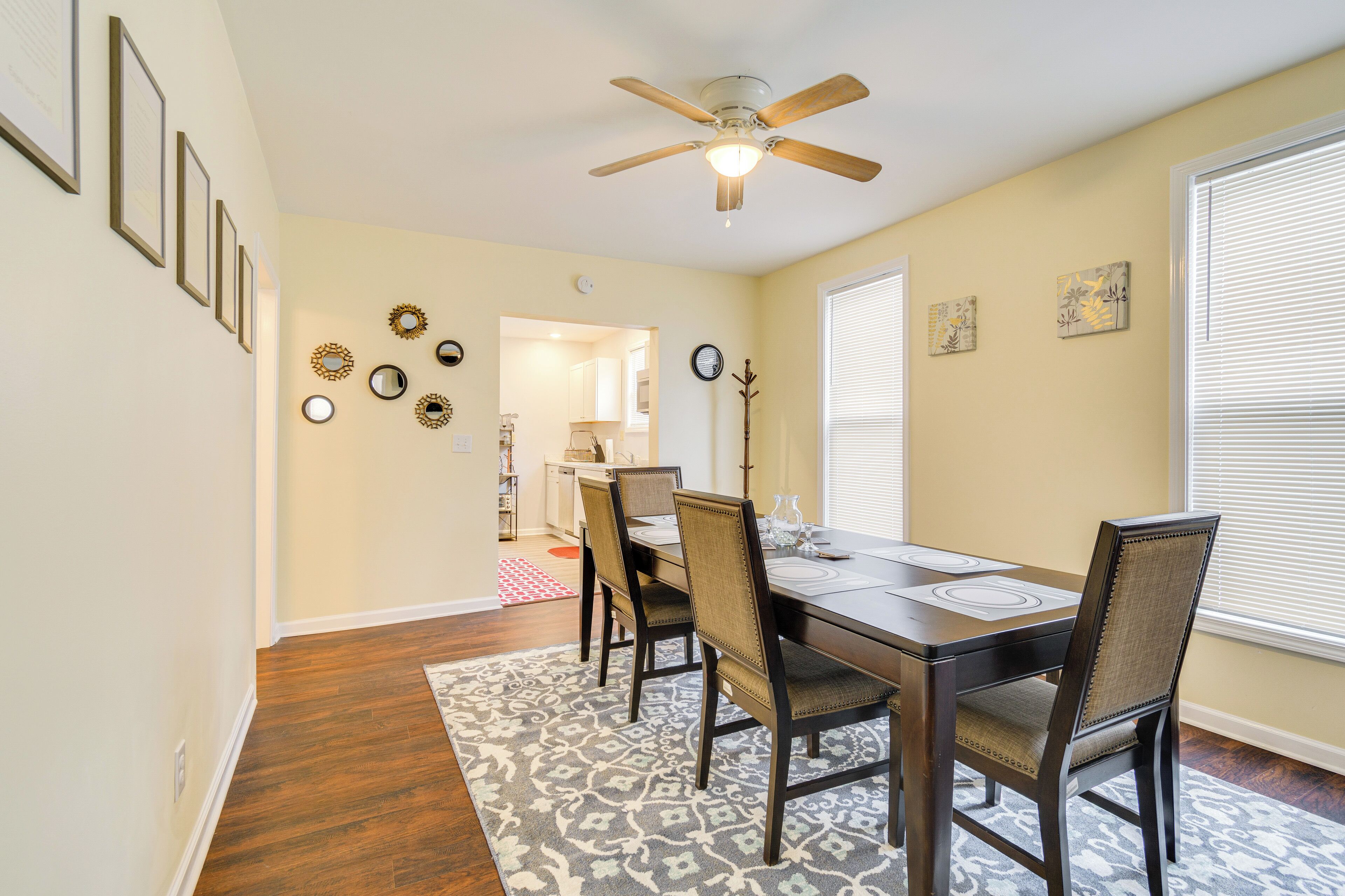 A dining area with a wooden table, four chairs, a ceiling fan, and a patterned rug.