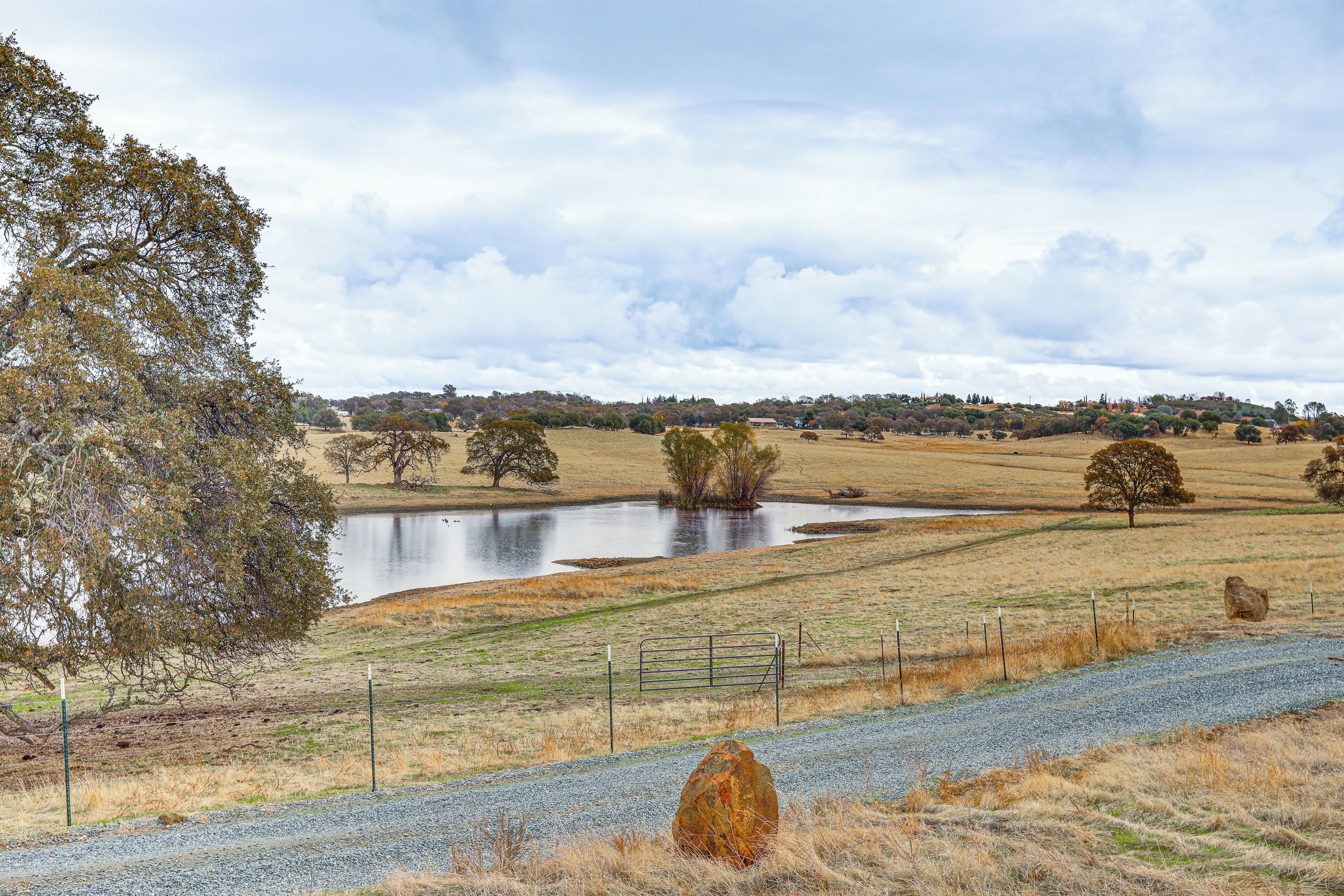 A rural landscape with a gravel path, a fenced area, and a body of water.