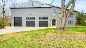 Una casa moderna de dos pisos con garaje, entrada para vehículos y un gran árbol en el jardín delantero.