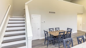 Un comedor con una mesa y sillas de madera, una escalera y una puerta.