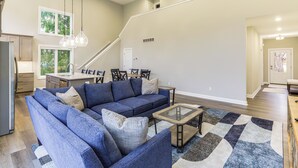 Amplia sala de estar con sofá modular, una mesa de centro de vidrio y un comedor con mesa y sillas.