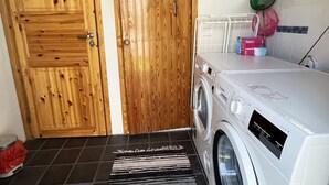 Un área de lavandería con lavadora, puertas de madera y suelo de baldosas.