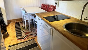 Una cocina compacta con lavavajillas, un lavabo, una mesa con sillas y una lámpara colgante roja.