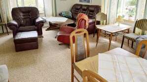 A living room with a brown leather sofa, a red armchair, a wooden table, and a patterned rug. - Cozy red cottage in the countryside outside Vimmerby I SE05038 (Gullringen)