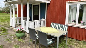 A red wooden house with a porch, a table with chairs, and a potted plant with flowers. - Cozy red cottage in the countryside outside Vimmerby I SE05038 (Gullringen)
