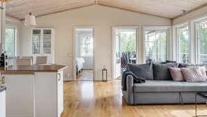 A spacious living area with a wooden ceiling, a grey sofa, and a kitchen area with white cabinets and a wooden countertop.
