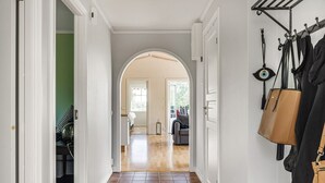 A hallway with a tiled floor, an archway leading to another room, and a coat rack with bags.