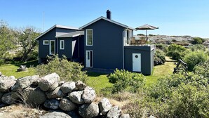 Una casa moderna de dos pisos con balcón, rodeada por un paisaje natural.