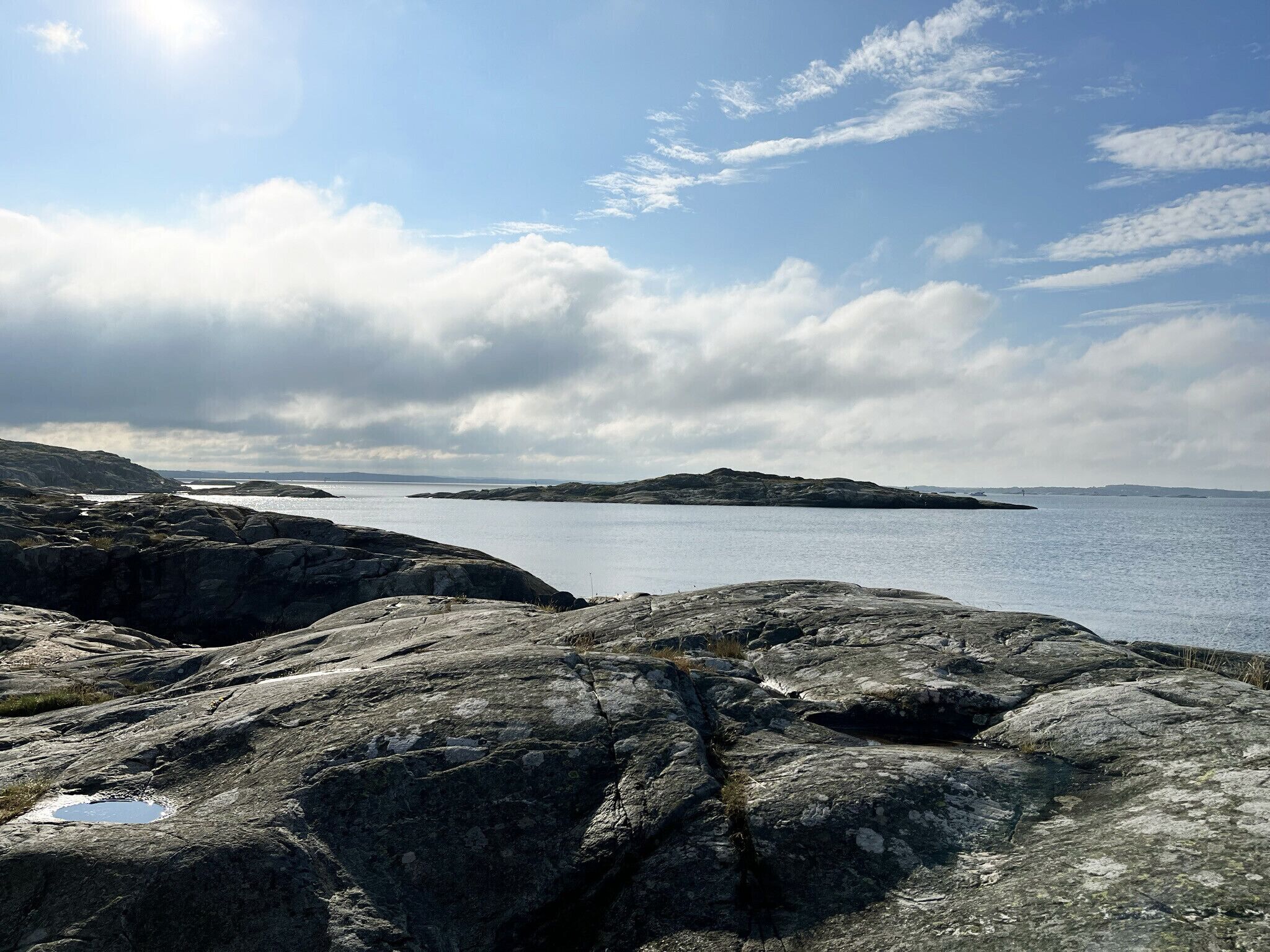 Un littoral rocheux, une mer calme et des îles lointaines sous un ciel partiellement nuageux.