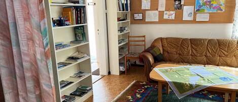 A cozy room with a brown leather sofa, a wooden chair, a small table with a map, and a bulletin board with papers and photos.