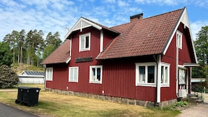 Ein rotes, zweistöckiges Haus mit geneigtem Dach, weißen Fensterrahmen und einer kleinen Veranda mit schwarzer Brüstung.