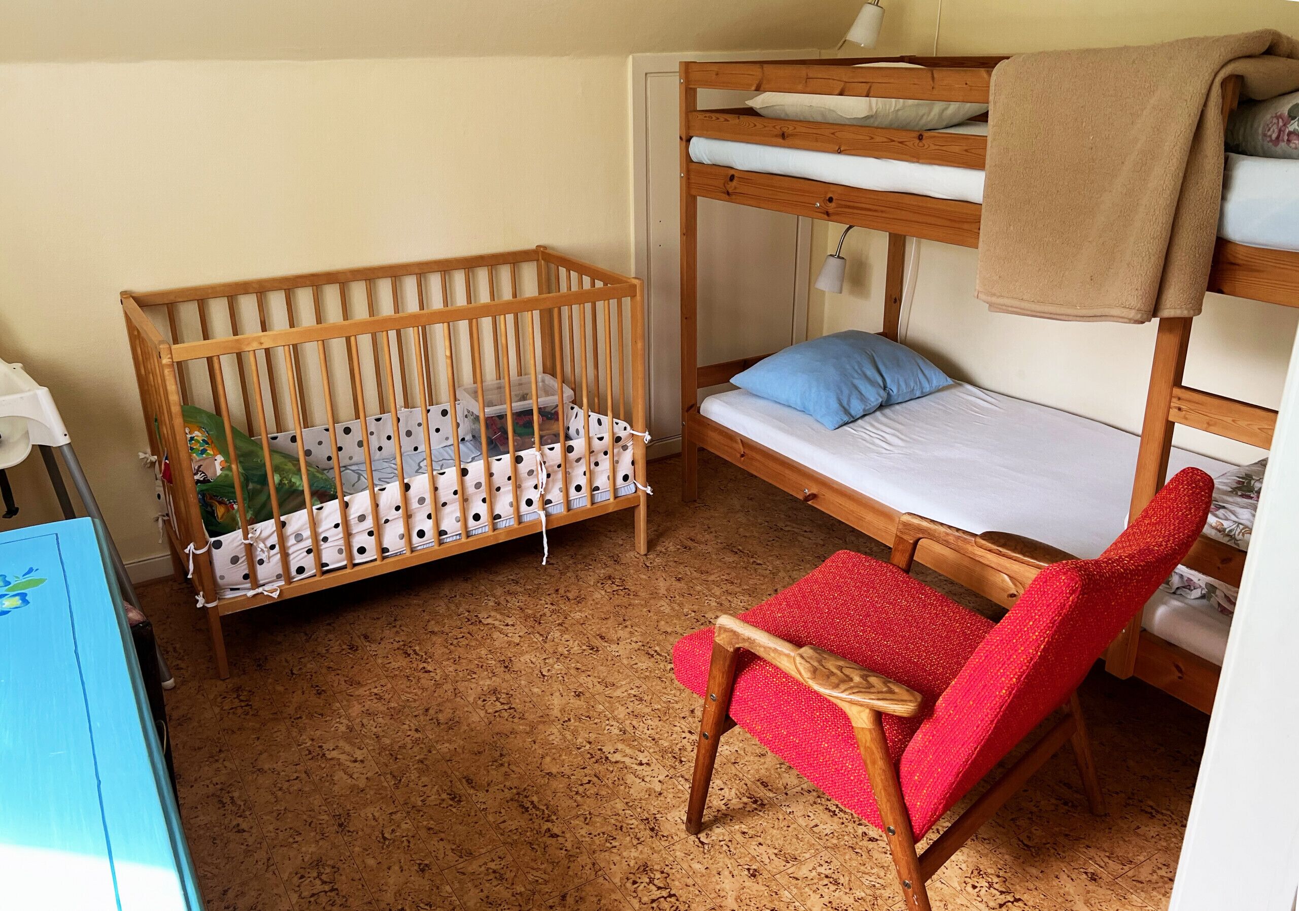 Een kamer met een ledikantje, een stapelbed en een rode stoel.