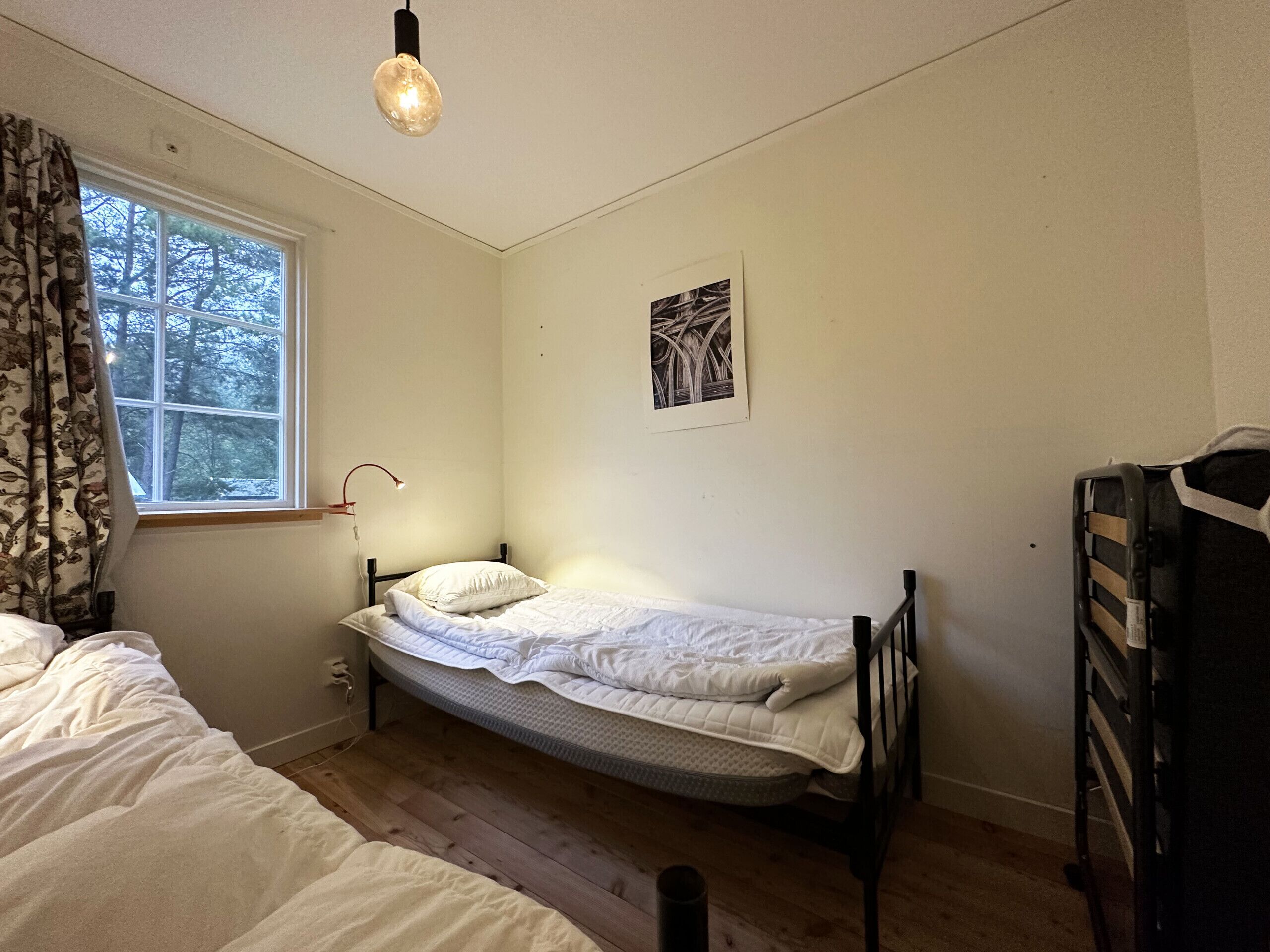 Un dormitorio con una cama individual, una ventana con cortinas, un cuadro en la pared y una lámpara de noche.