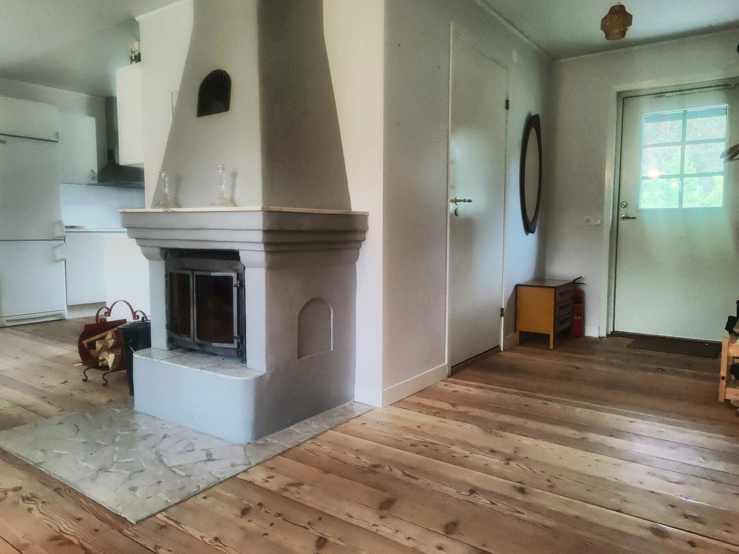 A room with a fireplace, wooden flooring, a door, and a window.