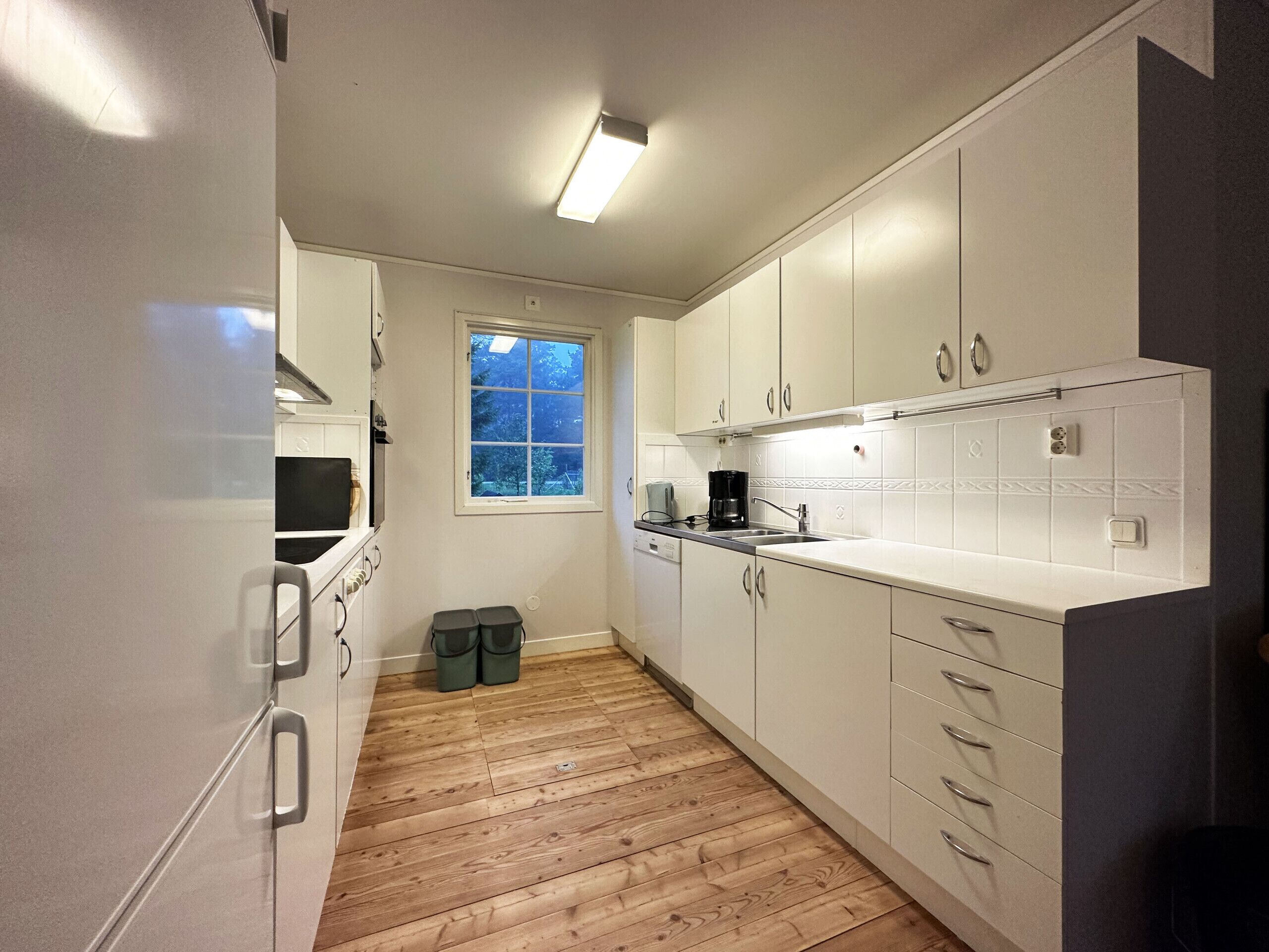 A compact kitchen with white cabinets, a window, and a wooden floor.