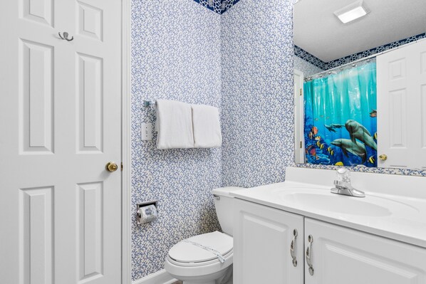 A bathroom with a white toilet, a sink with a mirror above it, and a shower curtain with an underwater scene. - Walk to Beach 4BR House w/ Resort Pool & Free Linens (Surfside Beach)